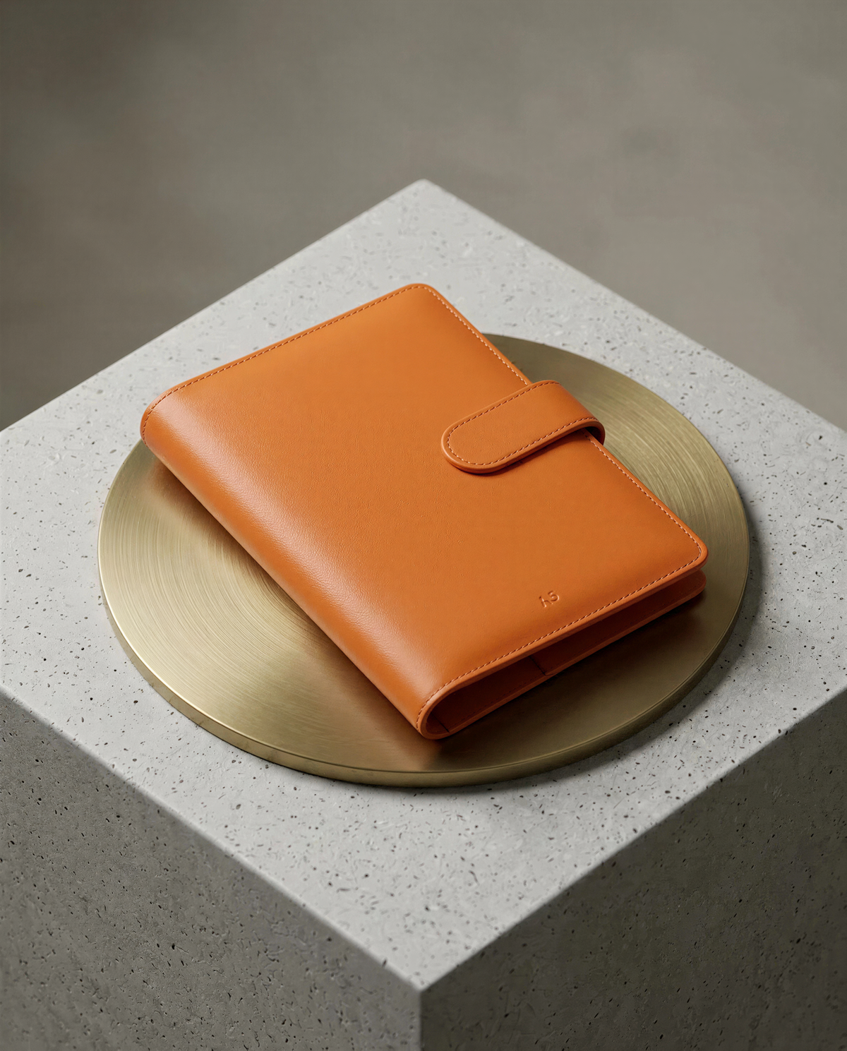 An orange leather wallet is placed on a round, gold-colored plate, which is placed on a gray, speckled surface.