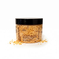A jar of citrus-flavored bath salt with a black lid, sitting on a white surface with scattered pieces around it.