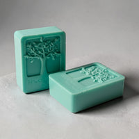 Two rectangular green soap bars with a tree design on them, sitting on a white surface.