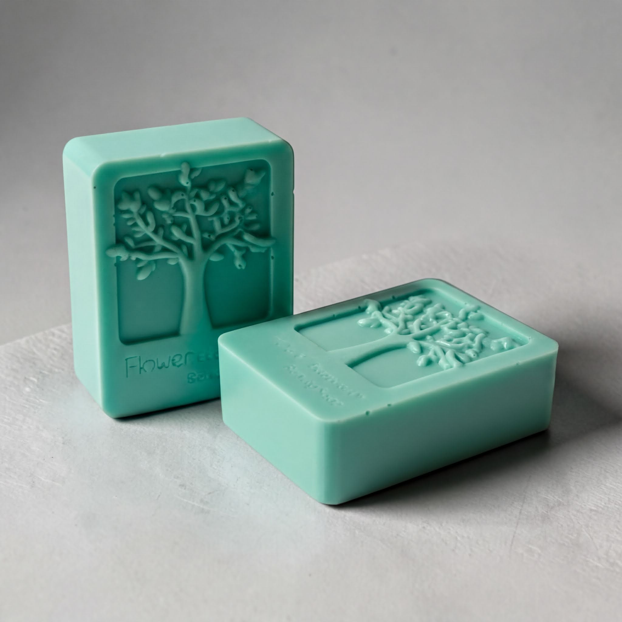 Two rectangular green soap bars with a tree design on them, sitting on a white surface.
