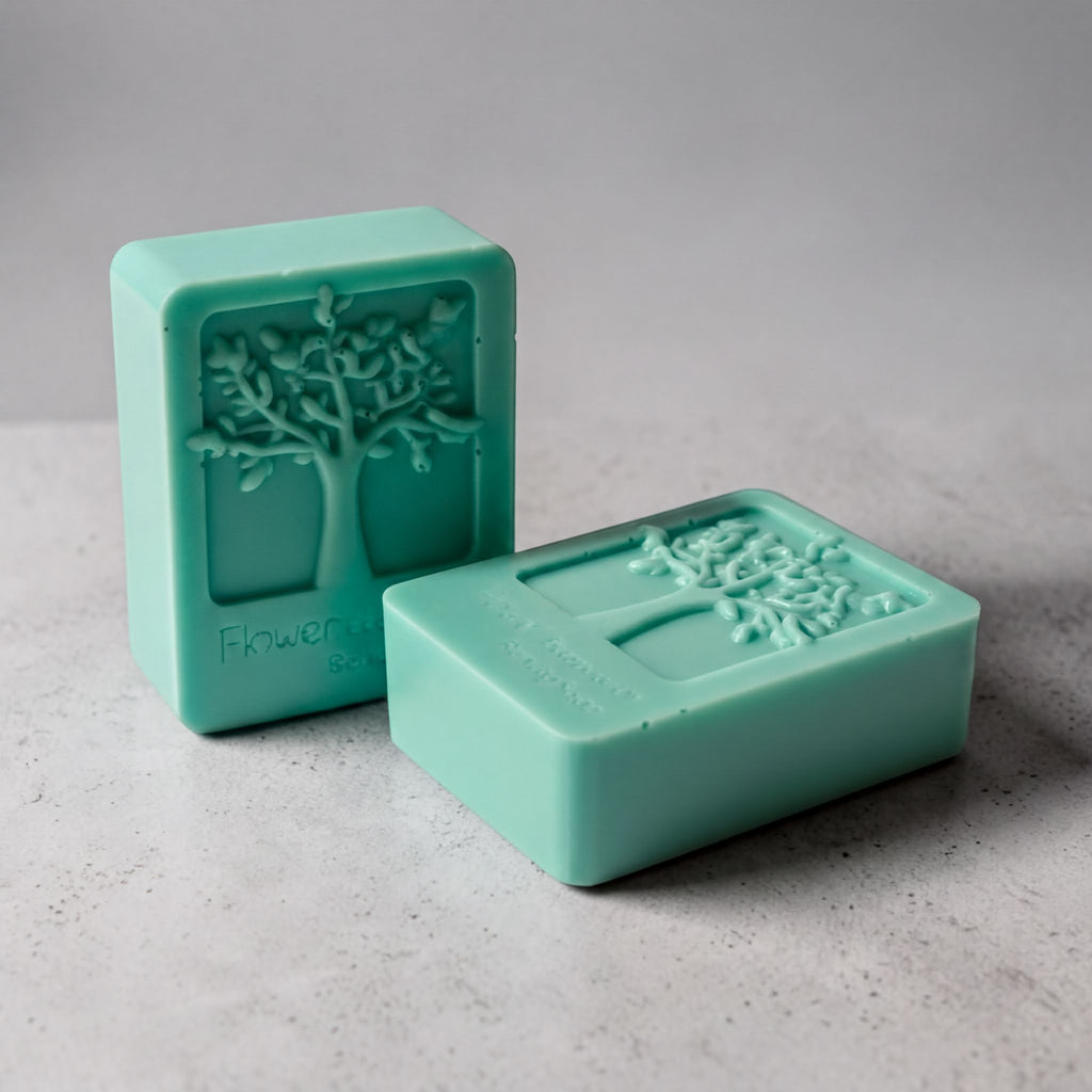 Two green rectangular soap bars with tree designs on them, placed on a gray surface.
