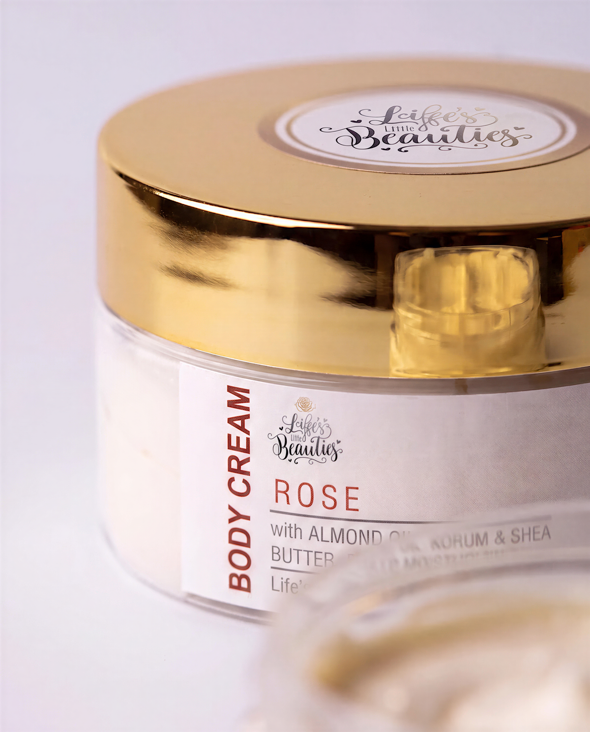 A jar of body cream with a gold lid, labeled "ROSE with Almond Oil, Kohen & Shea Butter".