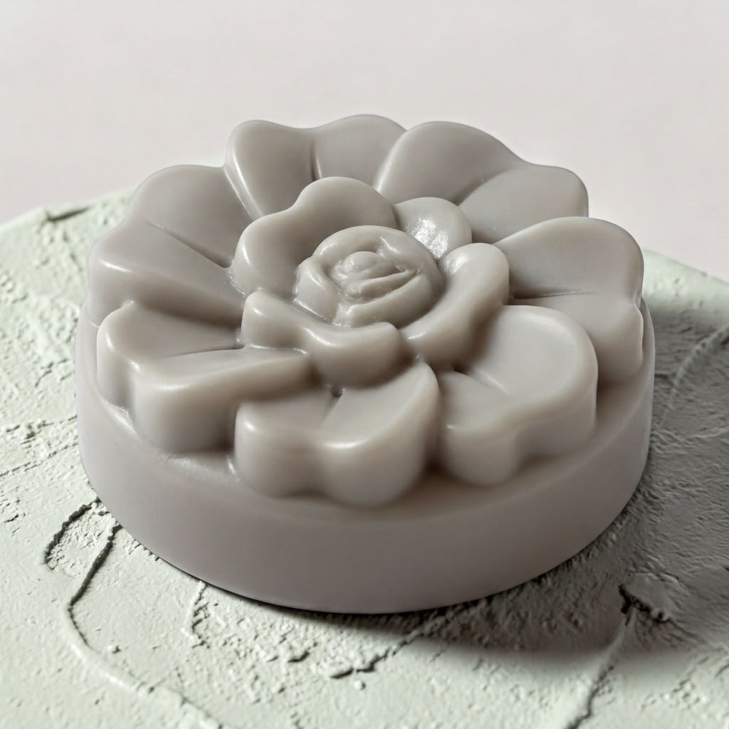 A gray, flower-shaped soap bar sits on a textured surface.