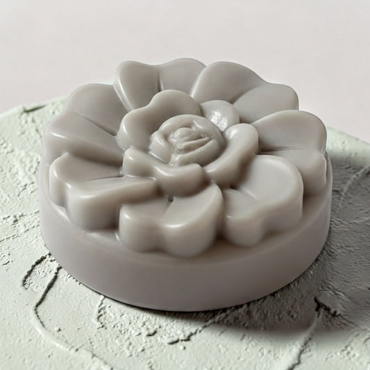 A gray, flower-shaped soap bar sits on a textured surface.