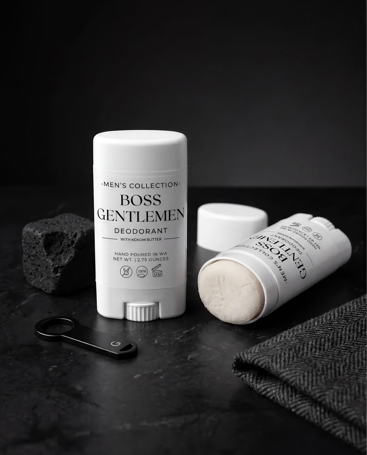 two deodorant sticks, one upright and one lying on its side, along with a black object and a black object with a white handle, all placed on a black surface.