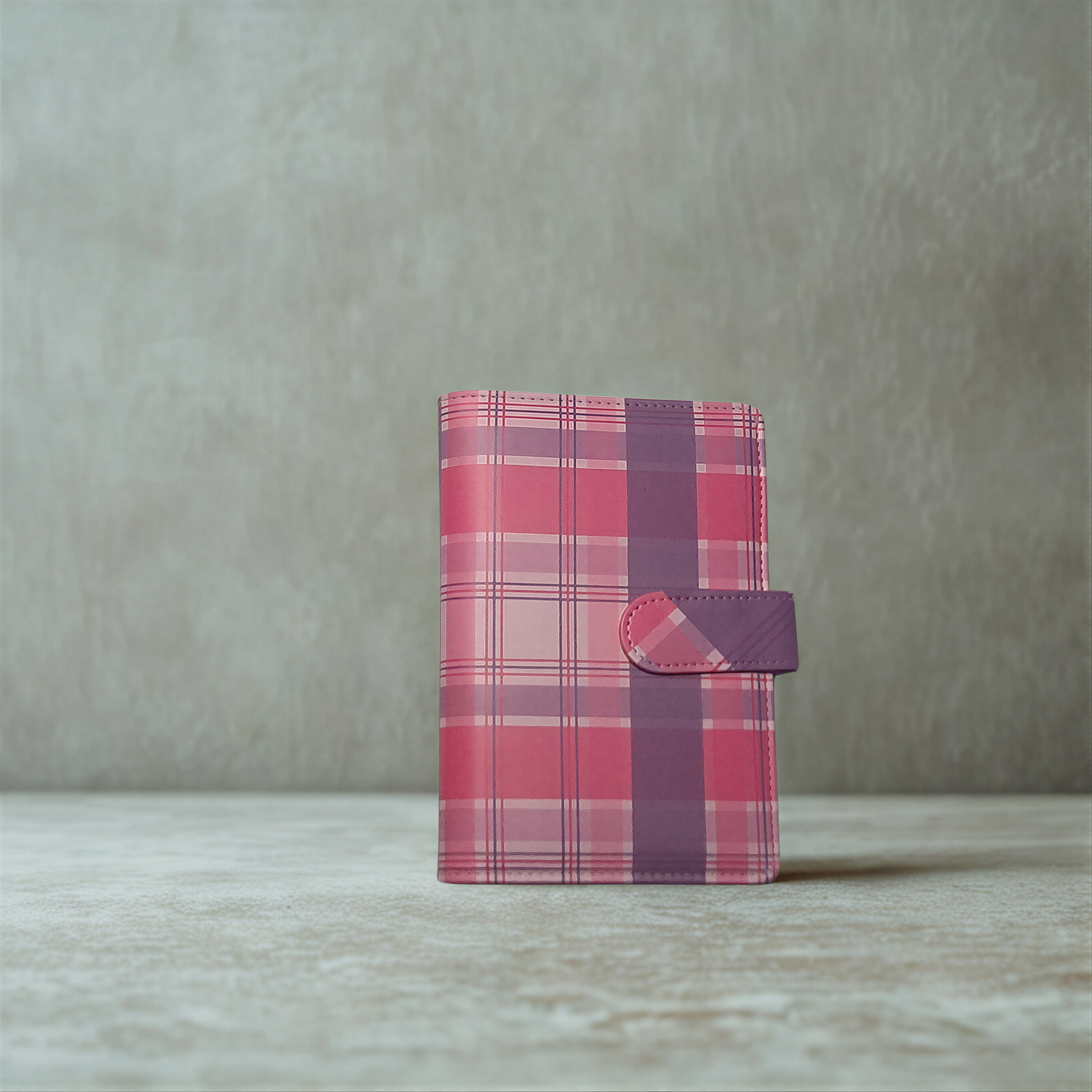Pink and purple plaid patterned wallet with snap closure on textured surface