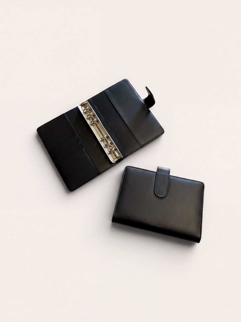 a black leather wallet and a binder with rings, both placed on a white background.