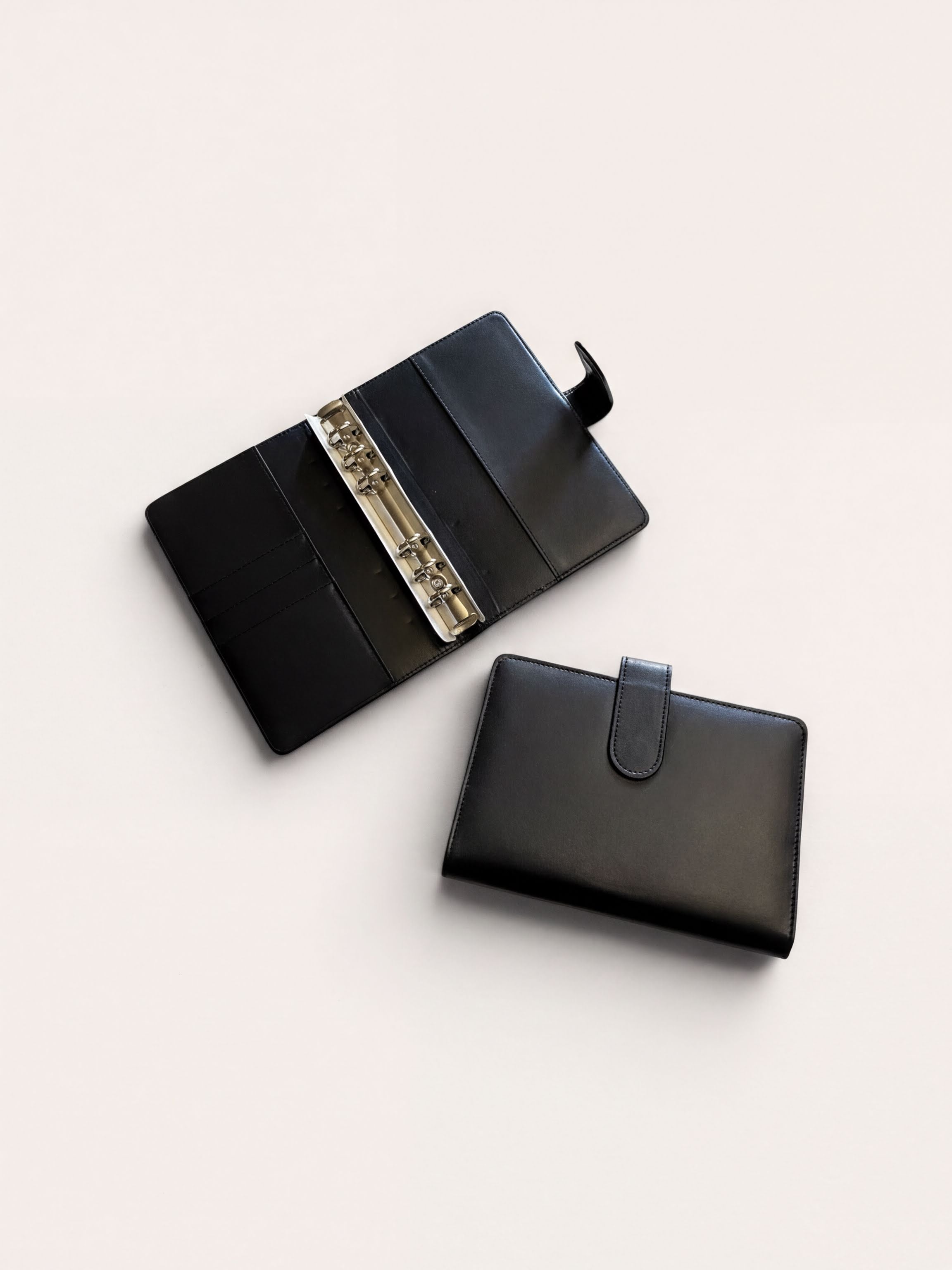 a black leather wallet and a binder with rings, both placed on a white background.