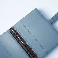 An open, light blue leather-like notebook or binder with a metal ring, resting on a white background.
