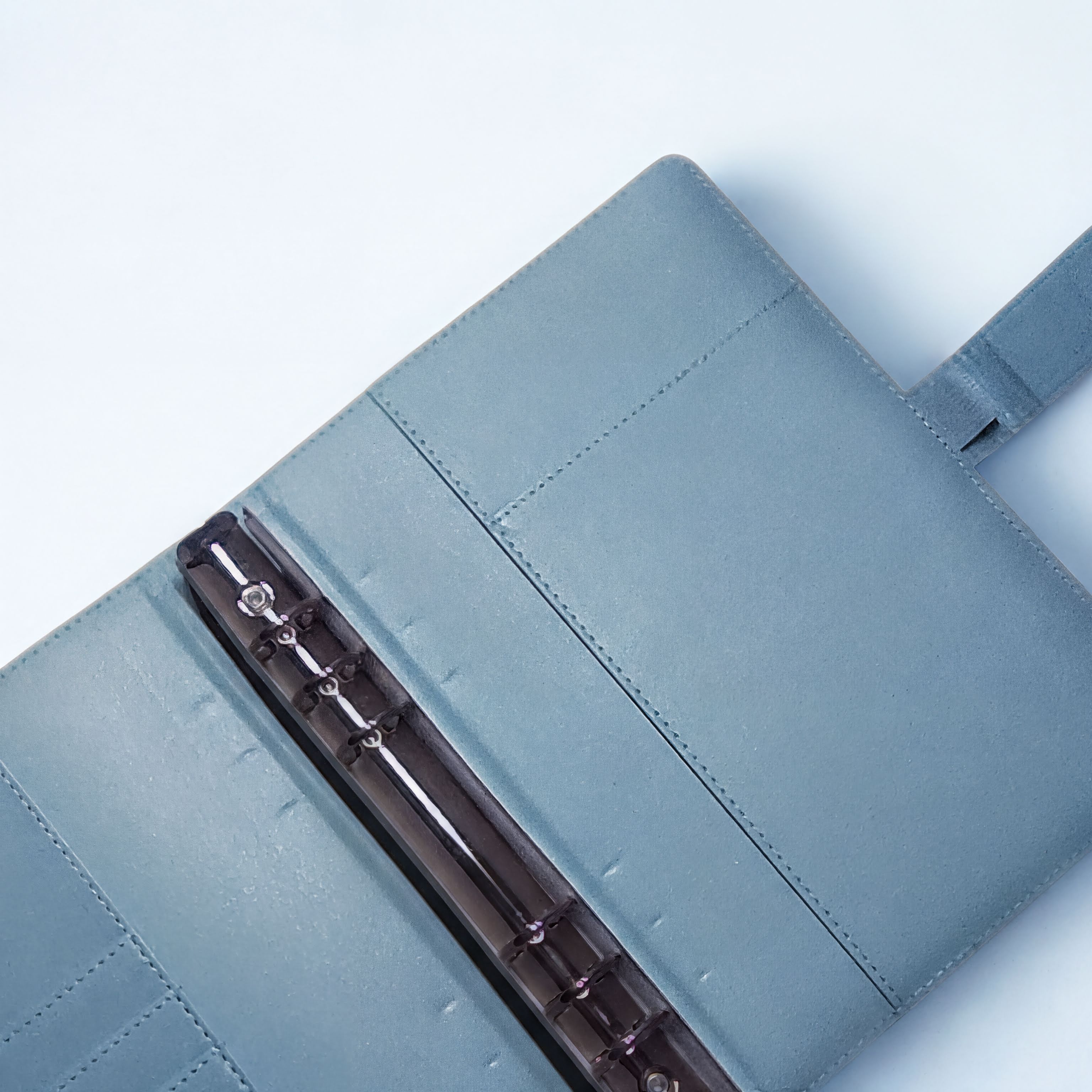 Blue leather notebook with black ring binder and stitched detailing on white background
