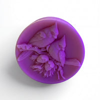 A purple wax sculpture of two birds perched on a branch, with flowers and leaves around them.