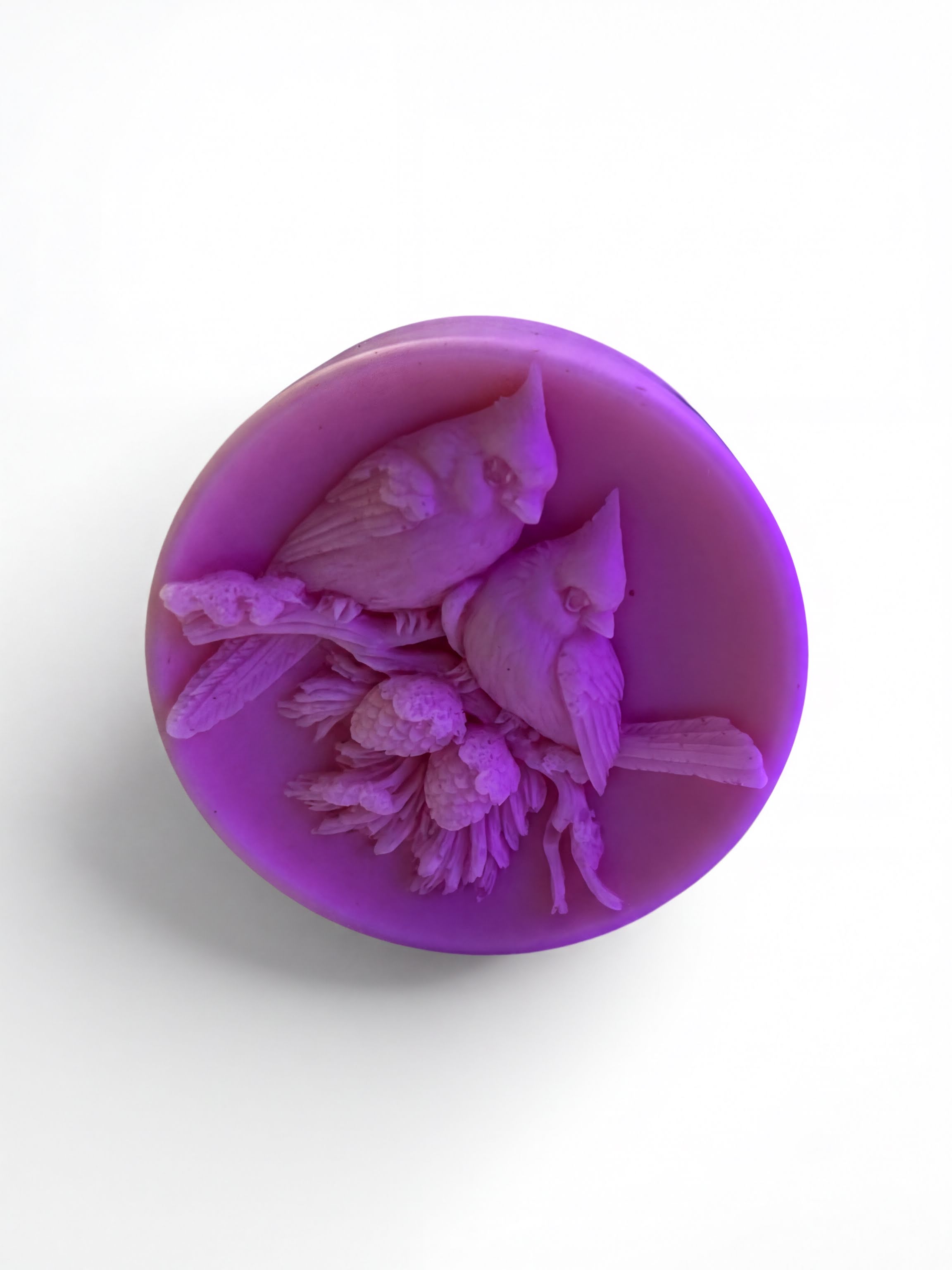 A purple wax sculpture of two birds perched on a branch, with flowers and leaves around them.