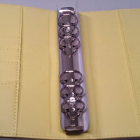 a metal binder with a yellow cover, containing a spiral-bound notebook or folder.