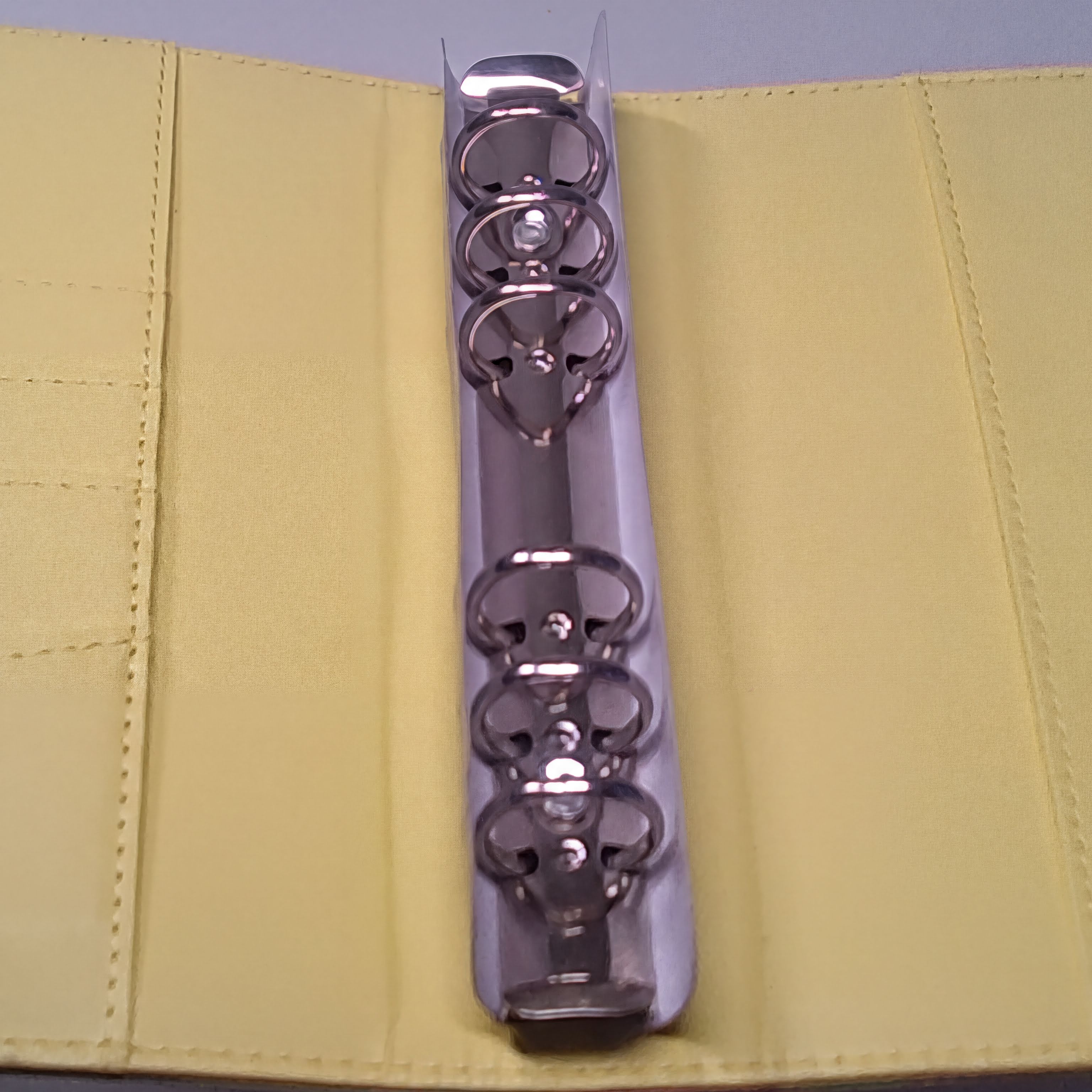 Shiny metal ring binder on pale yellow fabric background