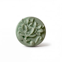 A round, green soap dish with a floral design featuring leaves and flowers.