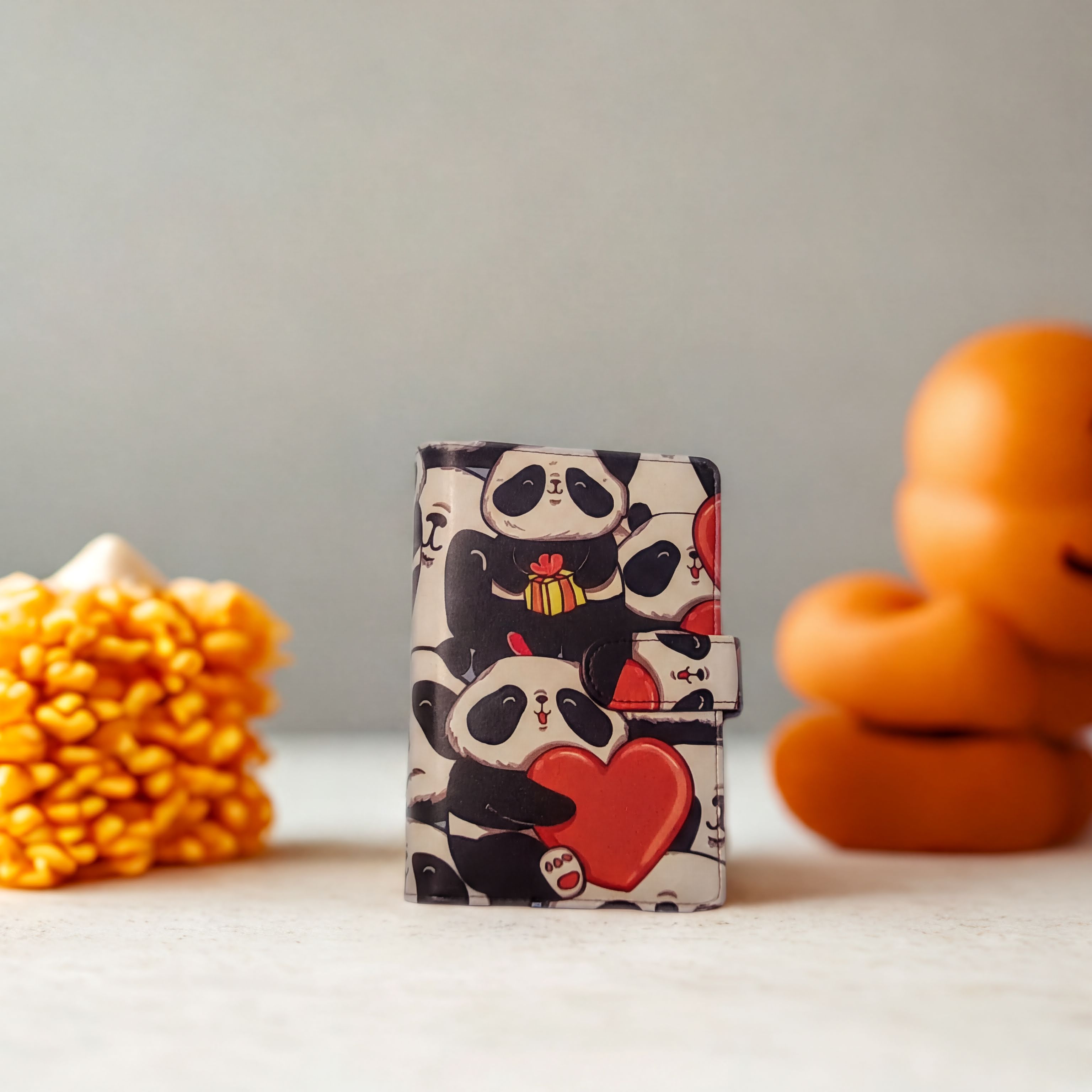Cute panda-patterned wallet with red hearts, standing on white surface beside orange decor