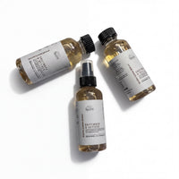 Three bottles of a brown liquid, possibly a hair spray or styling product, are arranged in a triangular formation on a white background.