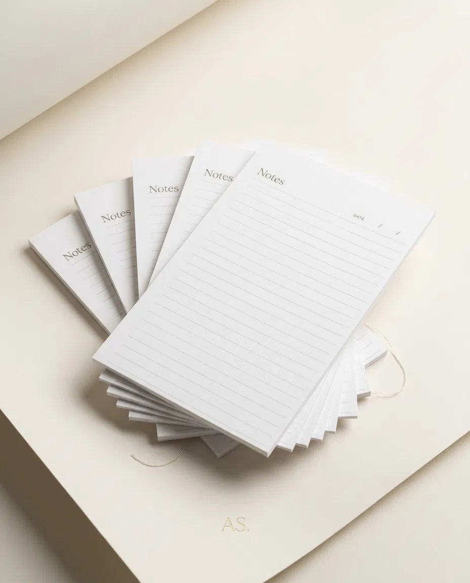 A stack of lined notepads with the word "Notes" written on them, arranged on a light-colored surface.