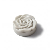 A white, round soap-like object with a flower-like design on it, sitting on a white background.