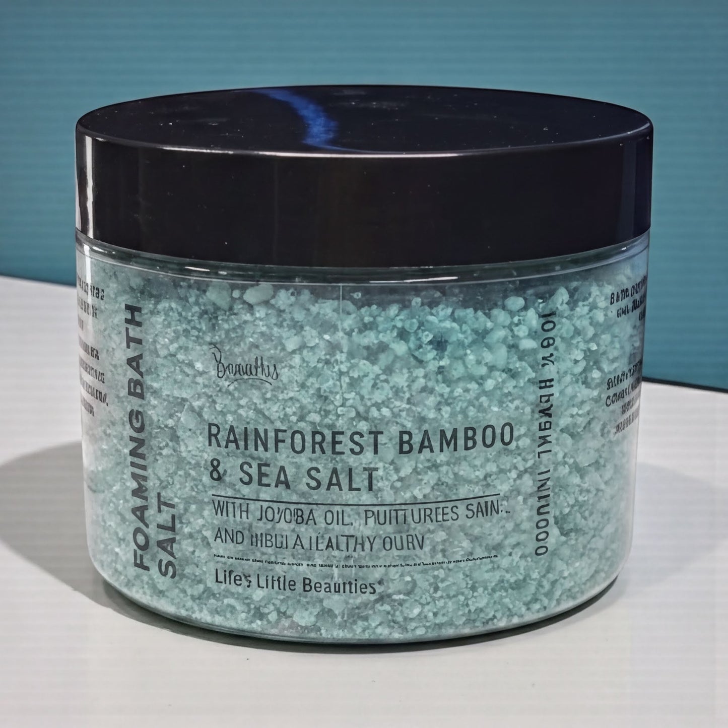 A jar of blue-green sea salt with a black lid, labeled as a "Rainforest Bamboo & Sea Salt" product.