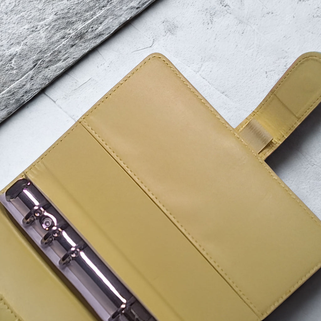Yellow leather journal with metal rings, resting on textured white surface